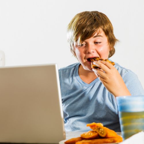overweight boy eating pizza while focused on a laptop